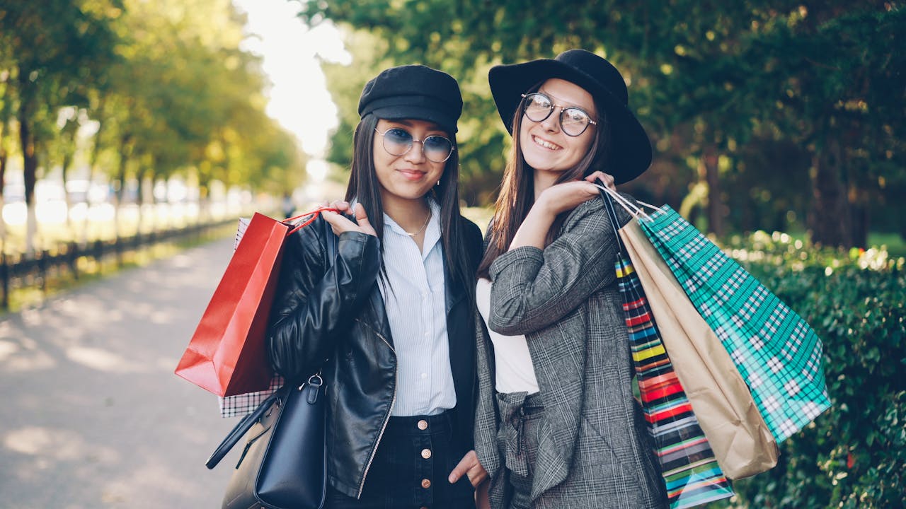 Two stylish women enjoy shopping outdoors with colorful bags and smiles.
