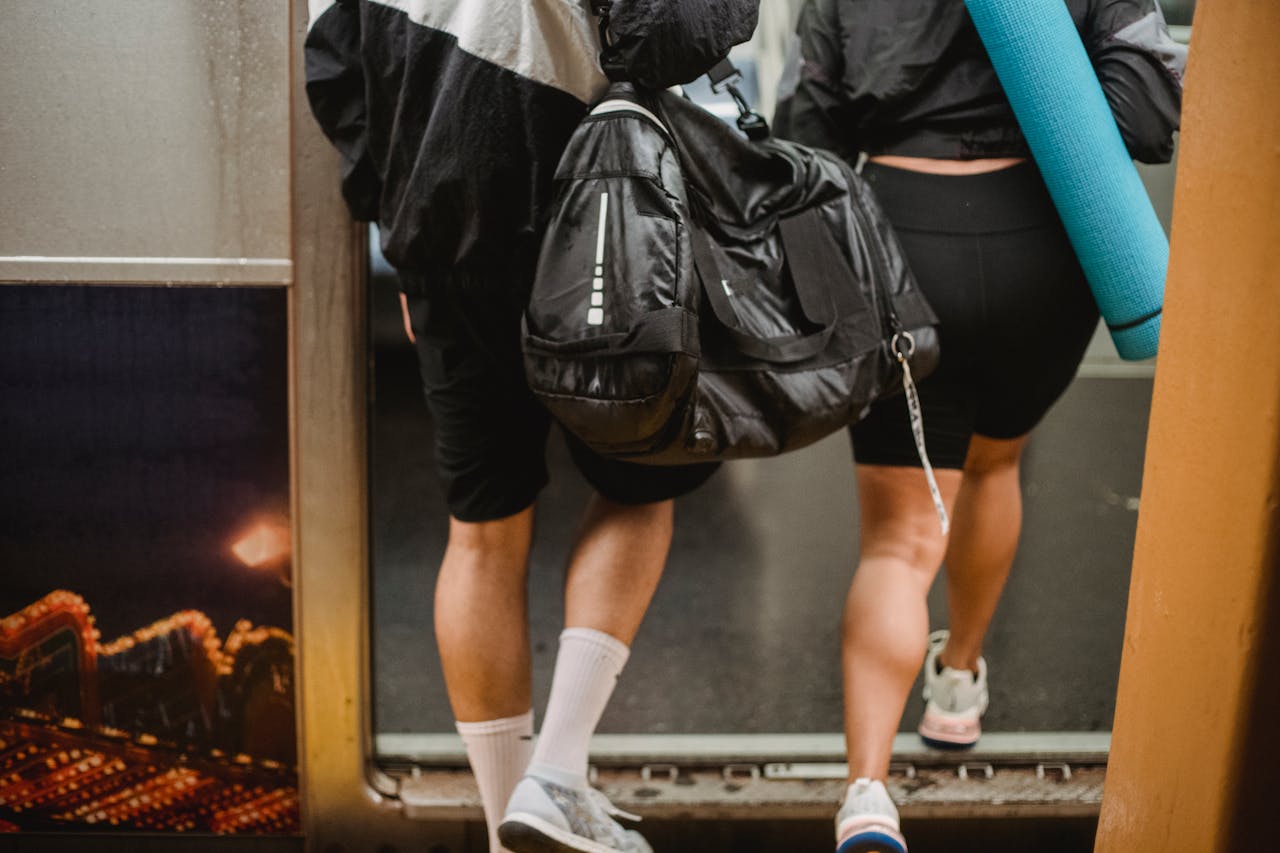 A man and woman boarding a subway train carrying a duffle bag and yoga mat, dressed in athletic gear.